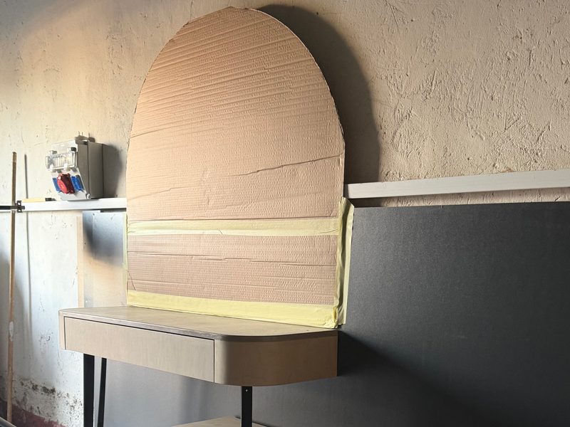 The same desk and drawer unit with a cardboard arch template on the wall