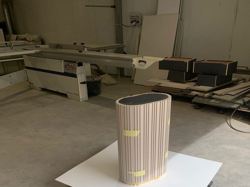 Fluted column cladding standing on a white board, workshop machines behind