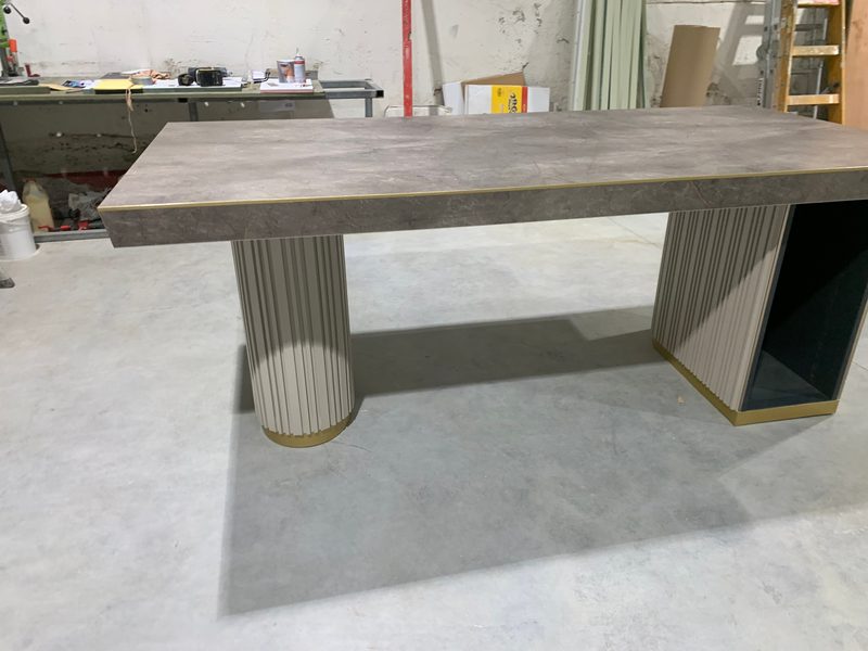 Table with a grey top and fluted pedestal legs, in the workshop