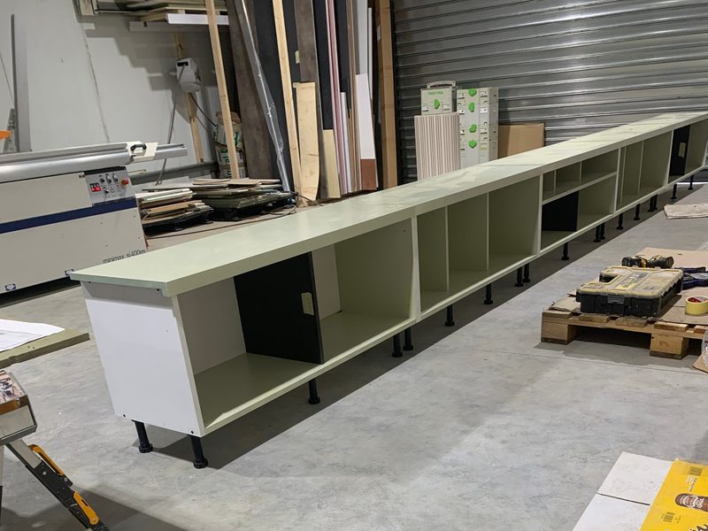 Long run of base cabinets on the workshop floor, cardboard laid alongside