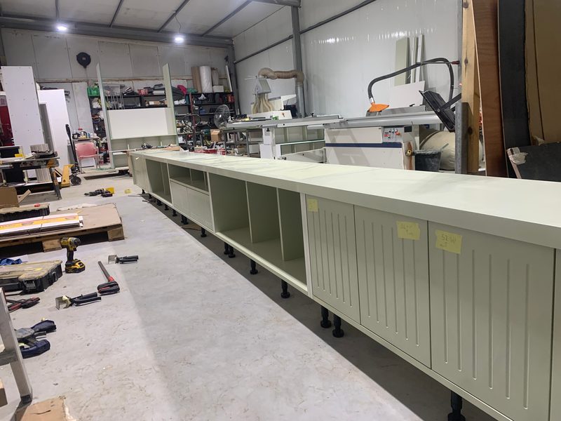 Long run of pale green cabinets with grooved doors, tools on the floor