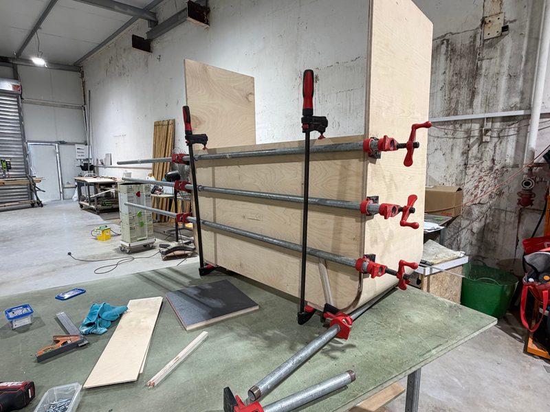 Panel held in long red pipe clamps on the work table