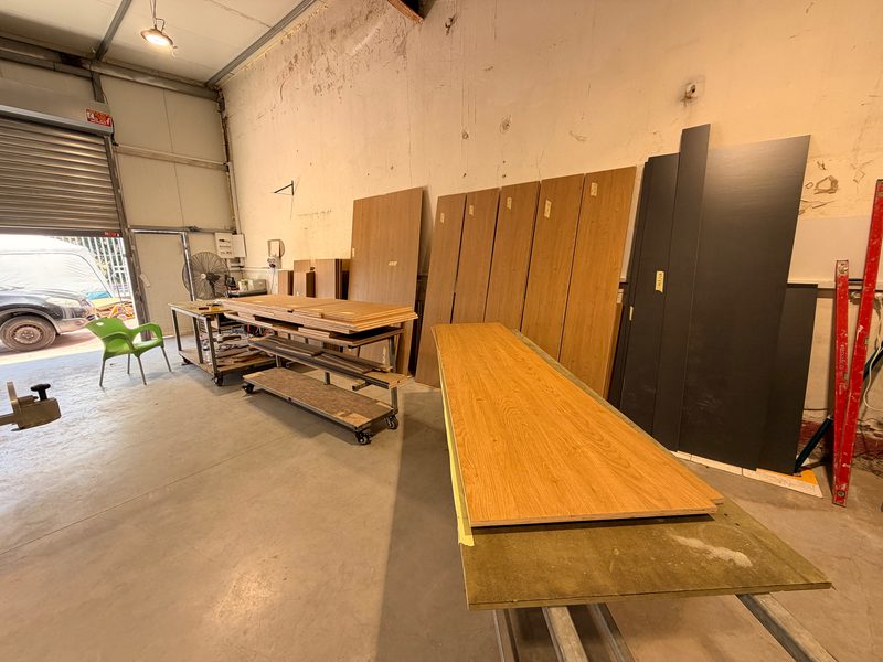 Wood-grain and black panels leaning on the workshop wall, a long panel on the bench