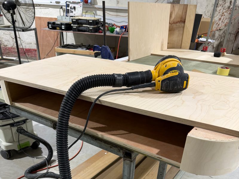 Sander with a dust hose resting on a cabinet with a curved end