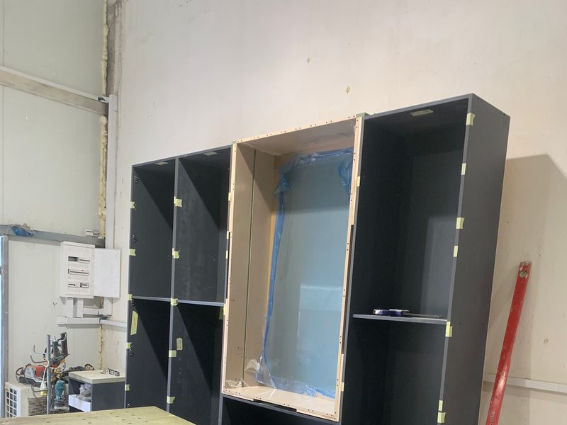 Tall dark unit with a panel still under protective film, next to a workbench