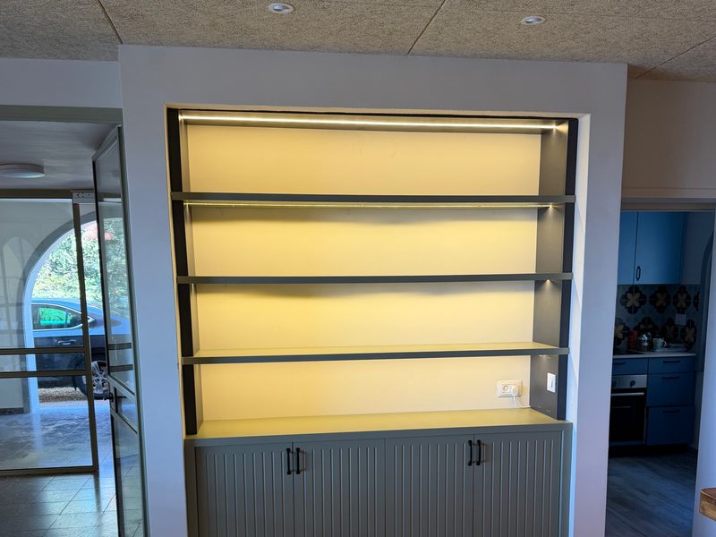 Built-in display shelves lit from behind, grooved grey cabinets below