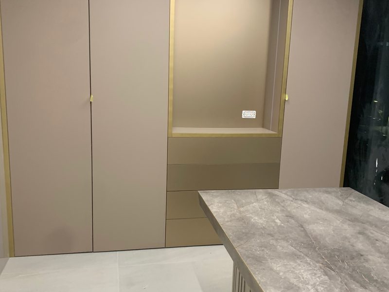 Wall of tall cabinets with gold trim, a table with a grooved base in front